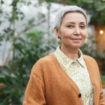 Older woman with short hair in front of foliage.